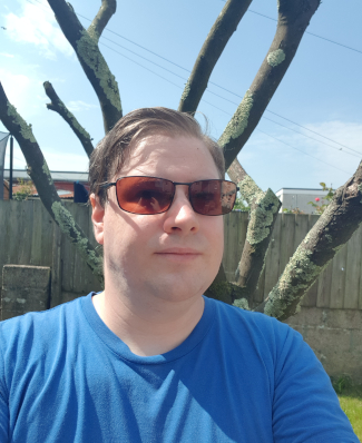 An image of Tom's head and shoulders in front of a bare-branched tree. He is wearing sunglasses and doing his best to look wistful, but he isn't very good at it.